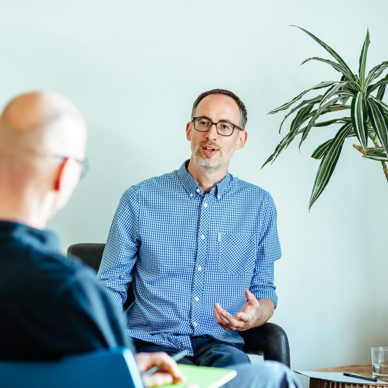 Daniel Craffonara spricht mit einer Klientin. Im Hintergrund ein Whiteboard voller Ideen. Auf dem Tisch bunte Notizen.