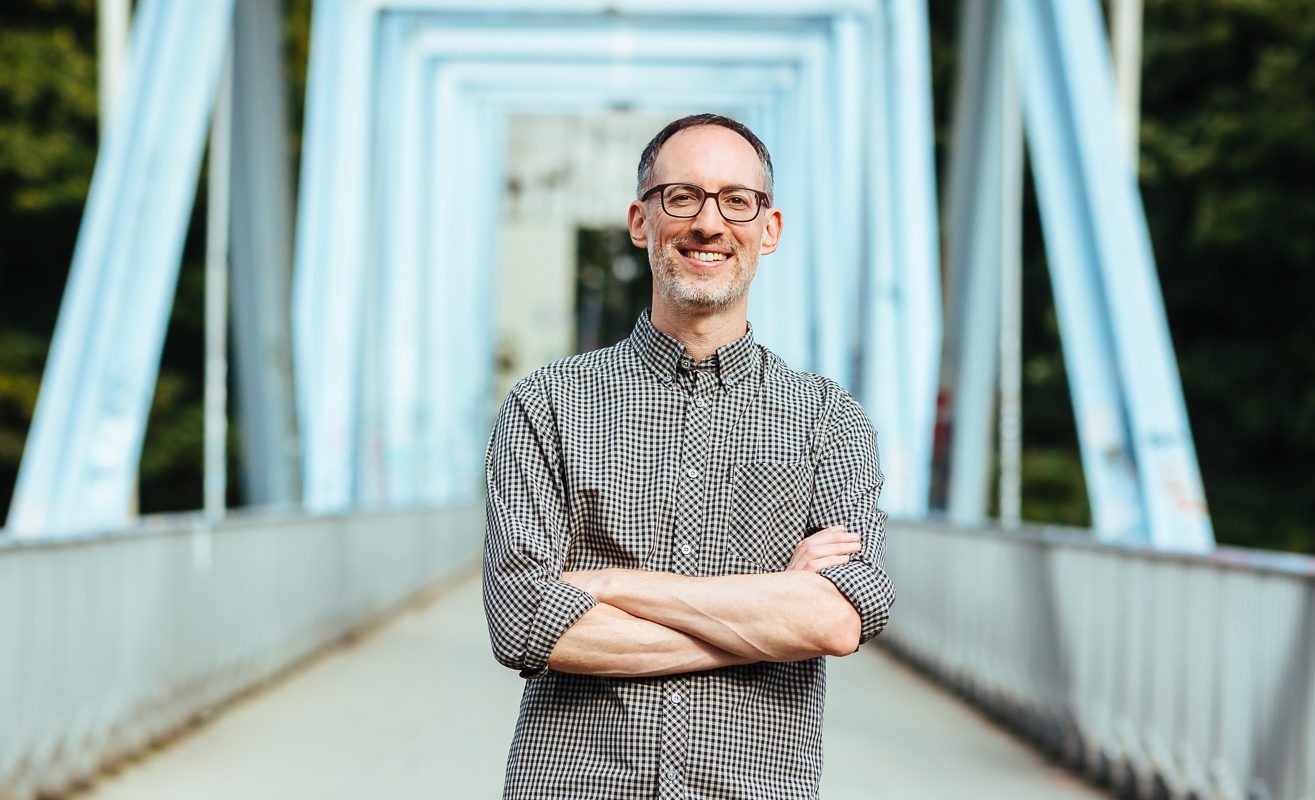 Daniel Craffonara, Coach für Führung, Entwicklung & Organisationskultur, auf einer modernen Stahlbrücke – offen, zugewandt, präsent.