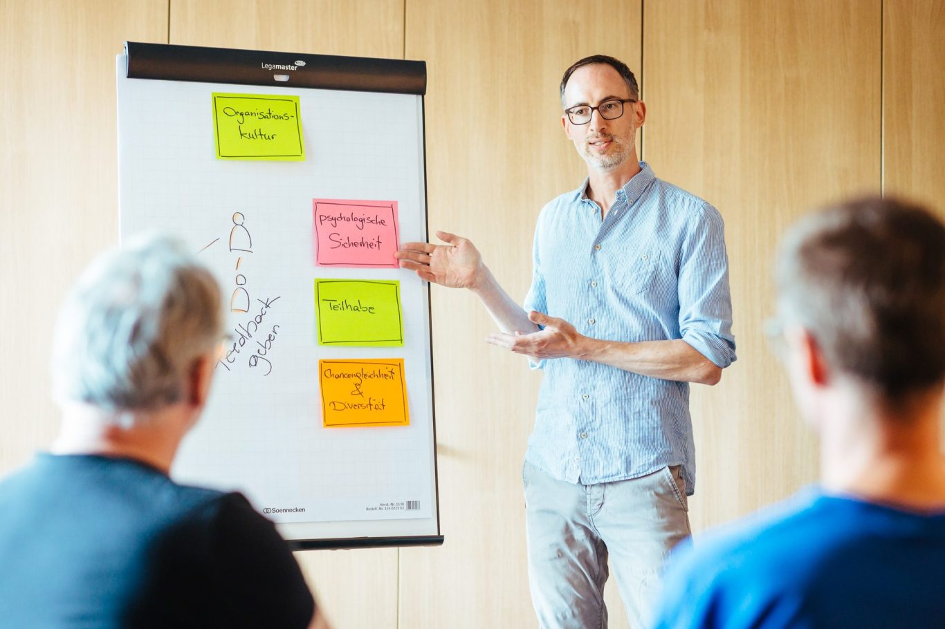Nahaufnahme von zwei Händen, eine hält einen Stift, während auf einem Tisch viele bunte Notizzettel liegen.
